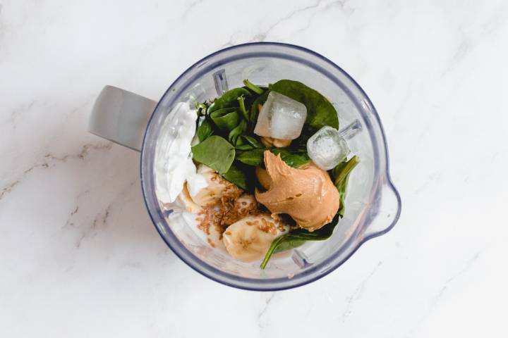 Banana, spinach, yogurt, peanut butter, ice cubes, and flax seeds in a blender.