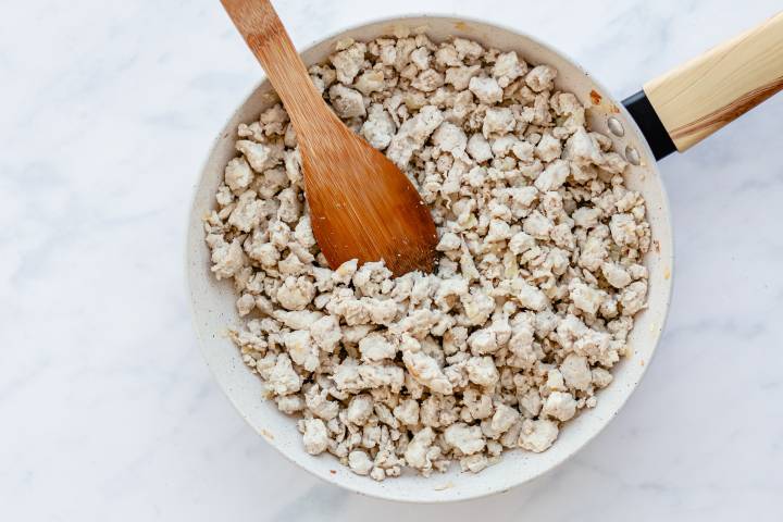 Ground turkey cooking in a white skillet with a wooden spoon.