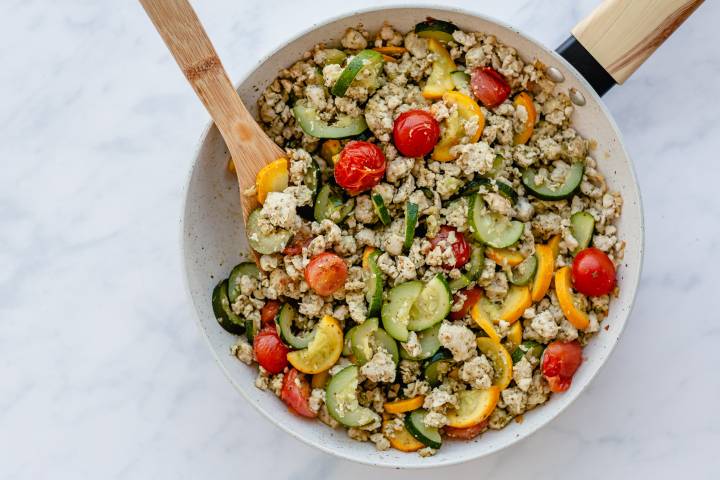 Pesto ground turkey with zucchini, yellow squash, and cherry tomatoes in a white skillet.
