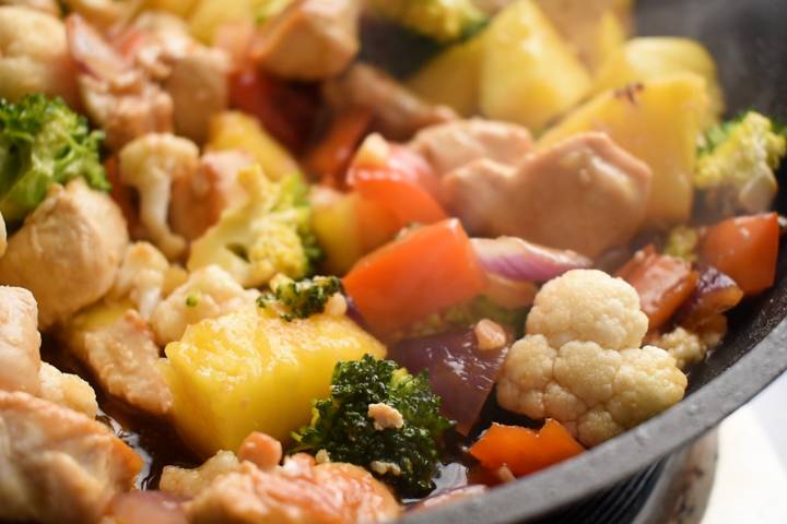 Cauliflower, broccoli, red bell peppers, and red onion cooking in a skillet.
