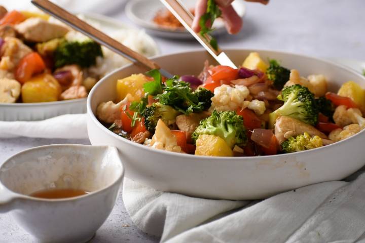Pineapple and chicken breast with broccoli, cauliflower, red pepper, and red onion in a bowl with stir fry sauce.