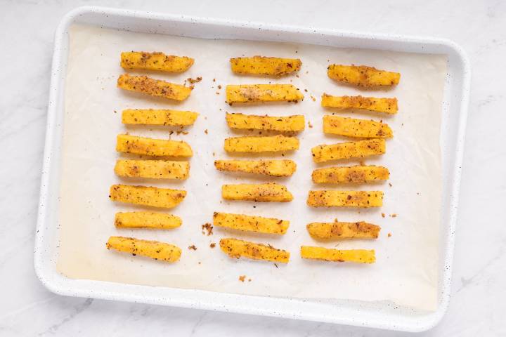 Baked polenta fries on a white baking sheet with parchment paper.