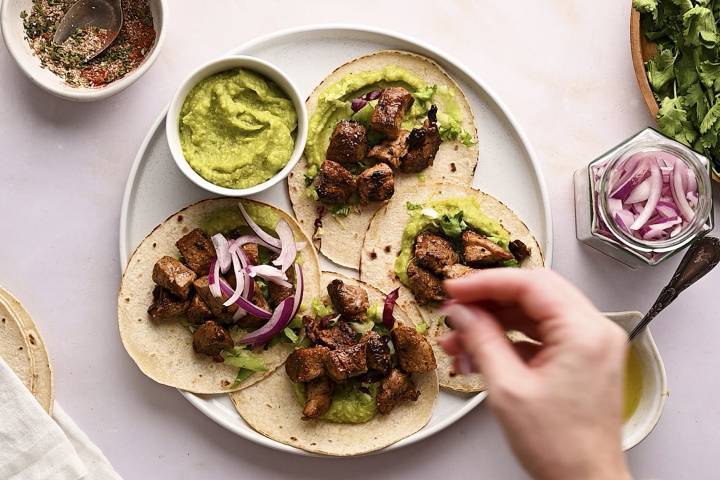 Red onion slices being added to pork tacos.