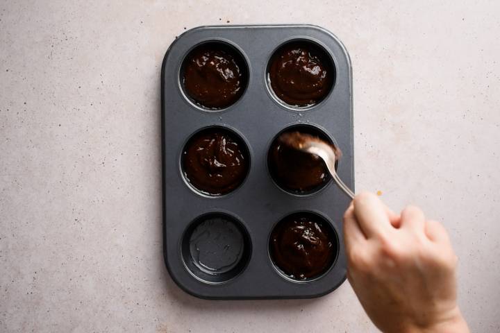 Pumpkin brownie batter being poured into a muffin tin.