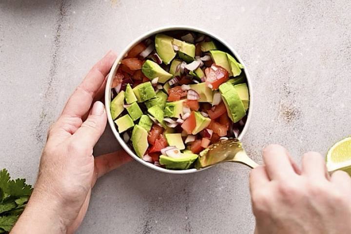 Avocado and pico de gallo being stirred together in a bowl.