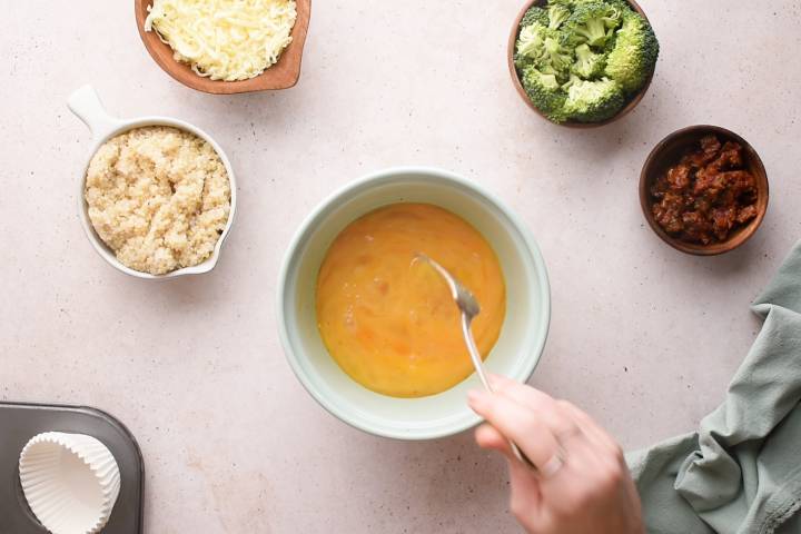 Eggs being whisked in a bowl with vegetables and cheese on the side.