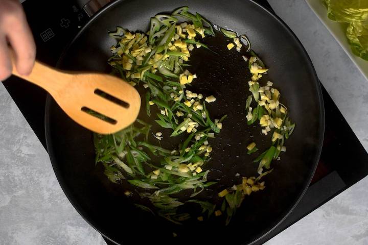 Ginger, green onions, and garlic being cooked in a skillet.