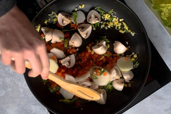 Mushrooms, red pepper, and water chestnuts being cooked in a skillet.