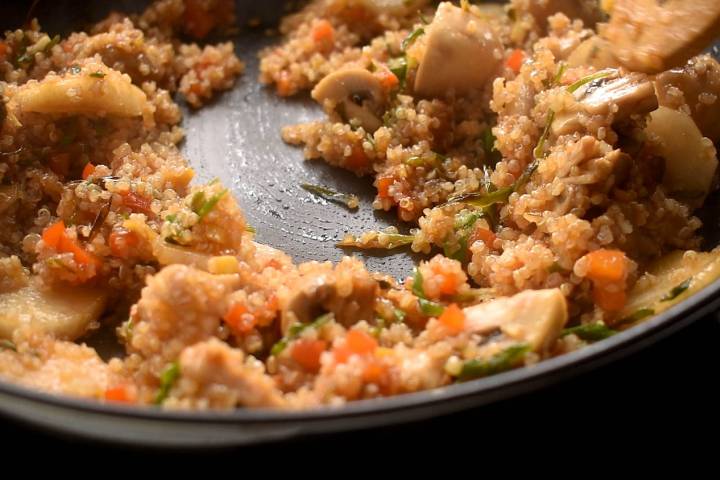 Quinoa in a stir fry sauce being stirred in a pan with vegetables.
