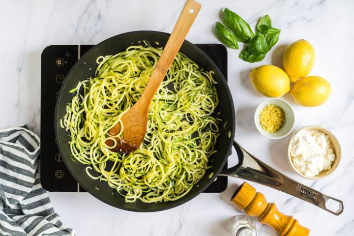 Zucchini noodles being cooked in olive oil in a skillet.