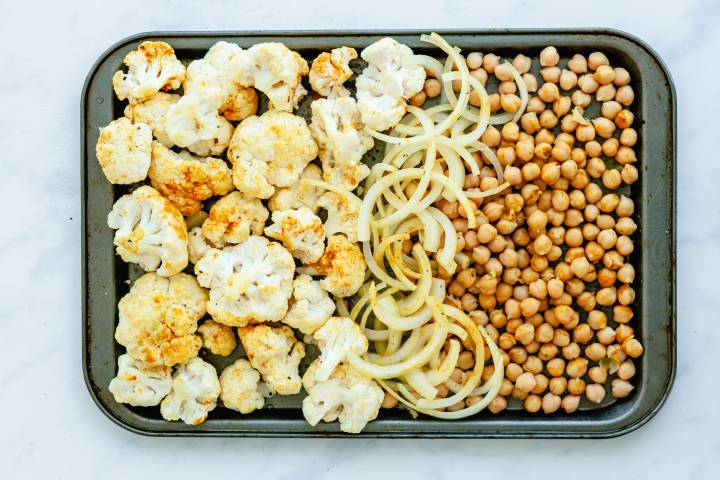 Cauliflower, chickpeas, and onions on a baking sheet with curry powder and spices.