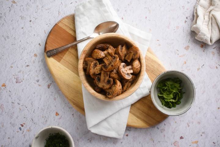 Roasted cremini mushrooms in a wooden bowl with fresh herbs, 