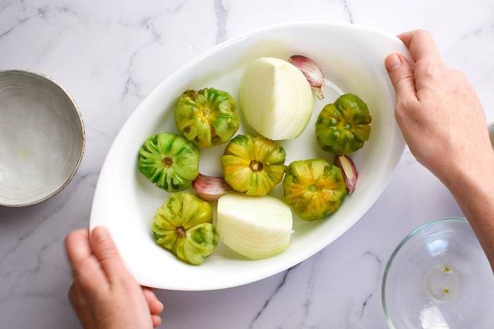 Tomatillos, onions, and garlic in a baking dish.
