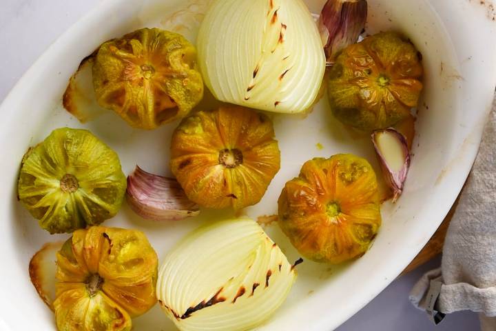 Roasted tomatillos, onions, and garlic in a baking dish.