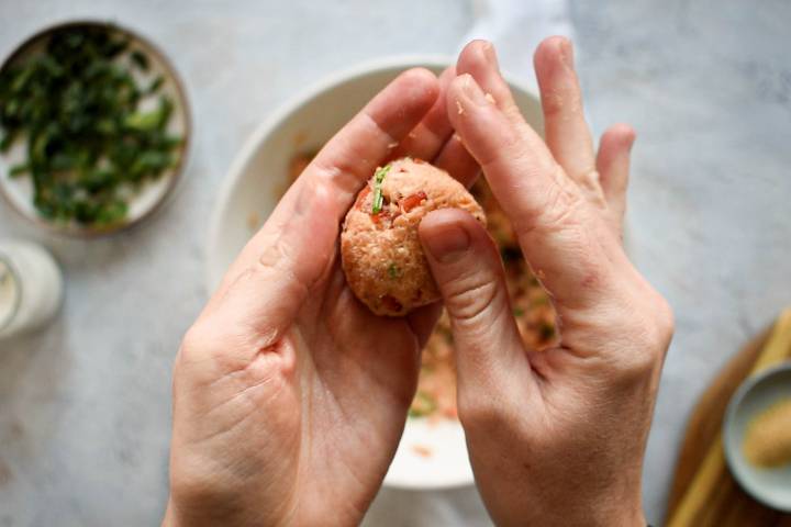 Salmon mixture being formed into patties by two hands.