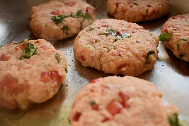 Salmon patties in a frying pan with olive oil.