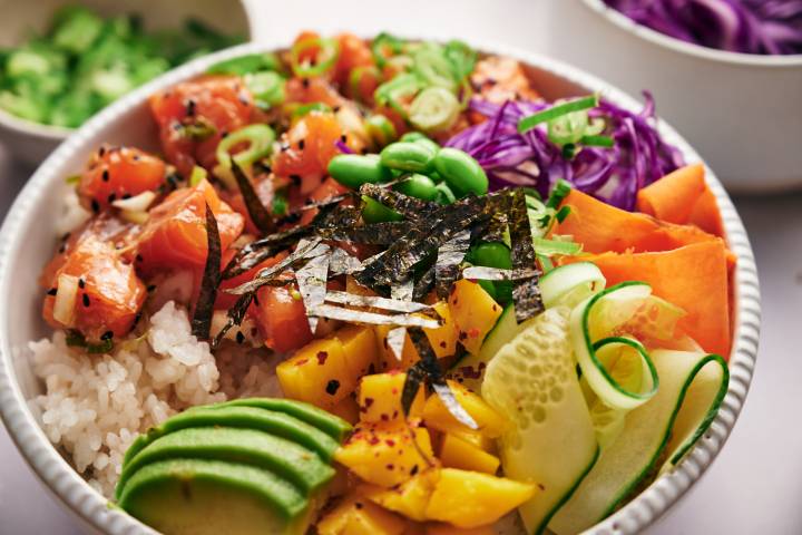 Poke salmon bowl with avocado, mango, cucumber, carrots, seaweed, and edamame.