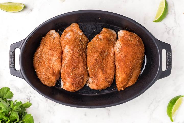 Chicken breast coated with cumin, chili powder, salt, pepper, and cayenne in a baking dish.