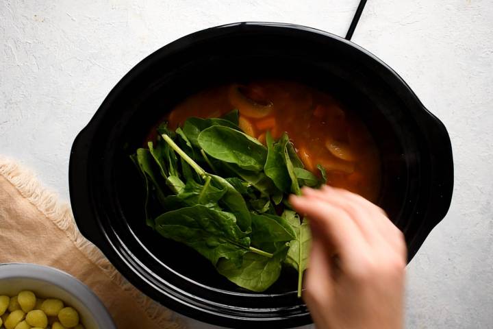 Spinach and potato gnocchi being added to a slow cooker soup.