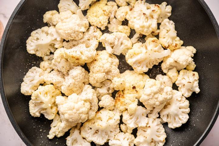 Close-up of cauliflower florets sizzling in a black frying pan. 
