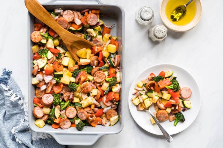 Baked chicken sausages with vegetables and potatoes in a baking dish and plate.