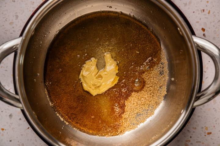 A stainless steel saucepan contains melted brown sugar, butter, and honey, creating a rich, caramel-like mixture. 