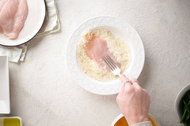 Chicken cutlets being breaded in a shallow bowl.