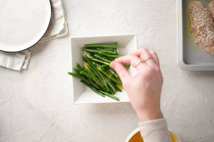 Green beans being tossed with olive oil, salt, and pepper.
