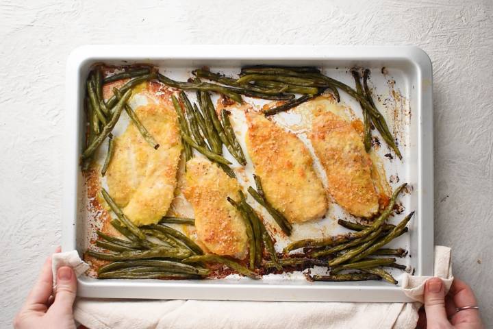Baked lemon pepper chicken cutlets on a sheet pan with roasted green beans.