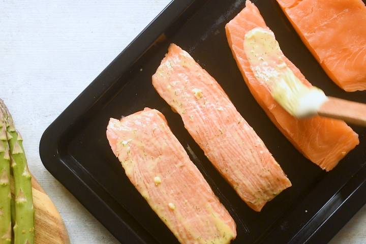 Salmon being brushed with lemon dill sauce.