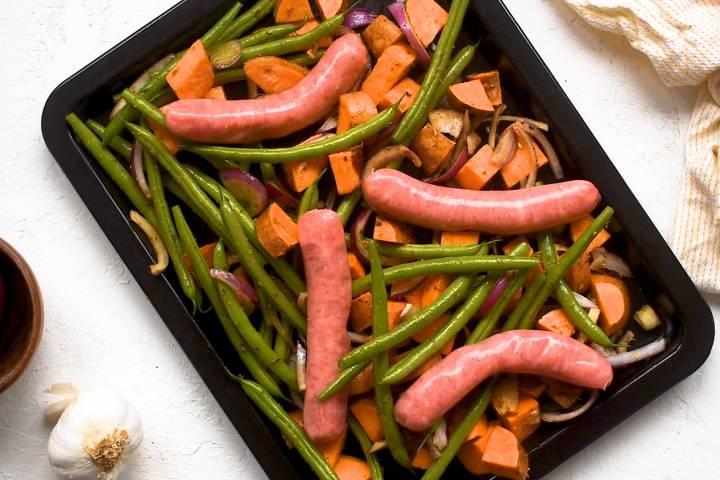 Sausages, sweet potatoes, and green beans spread out on a sheet pan.