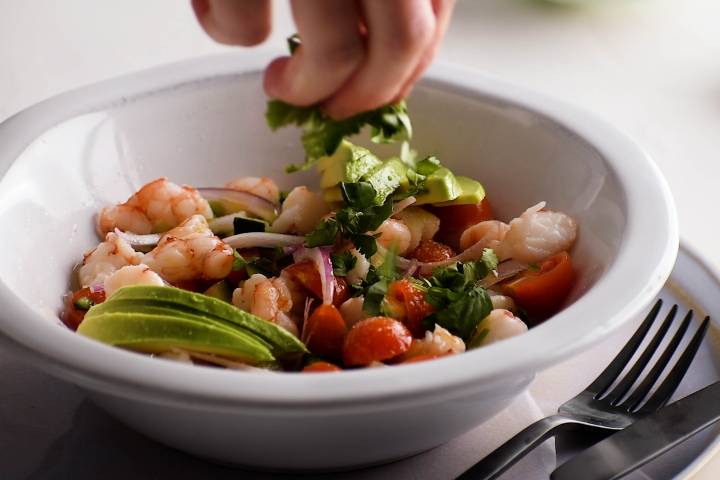Cilantro being added to shrimp ceviche in a bowl.