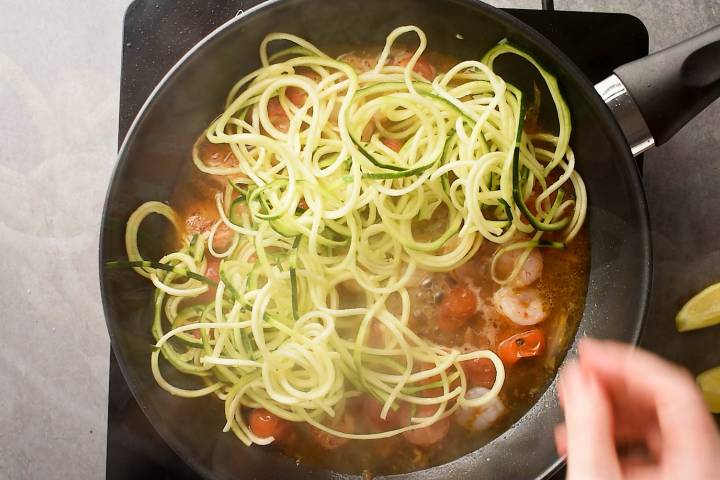 Zucchini noodles being added to shrimp scampi.
