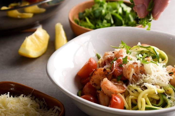 Parmesan cheese and parsley being sprinkled over scampi with shrimp.
