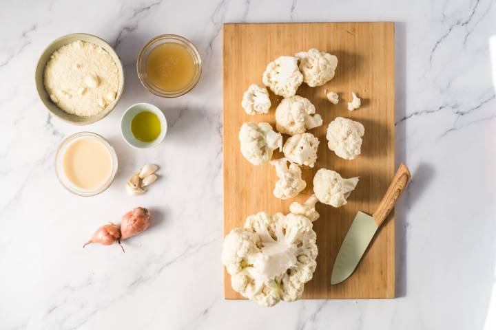 Cauliflower being cut into florets on a cutting board.