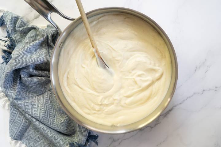 Creamy cauliflower alfredo sauce in a pan with a wooden spoon.