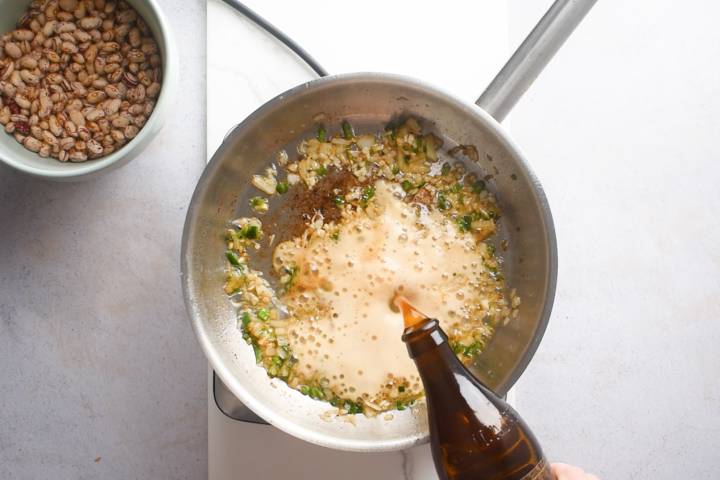 Jalapenos, onion, and beer cooking in a skillet.