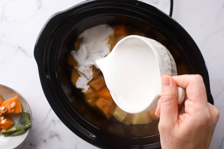 Coconut milk being added to a slow cooker full of butternut squash soup.