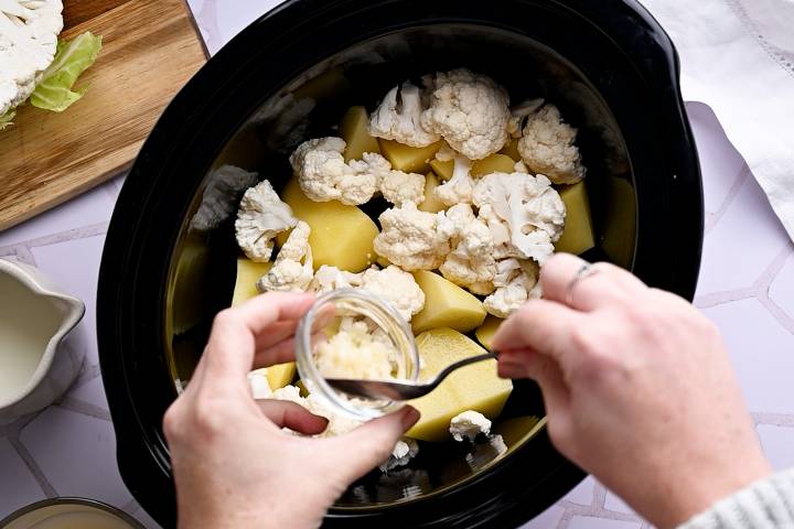 Garlic being added to a slow cooker with potatoes and cauliflower.