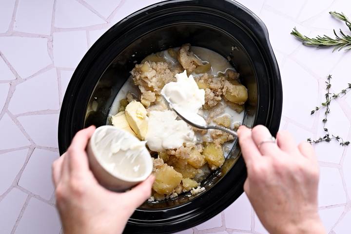 Butter being added to potatoes and cauliflower in a slow cooker.