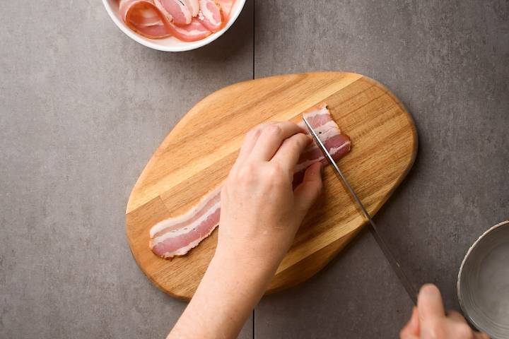Bacon being cut into small pieces in a cutting board.