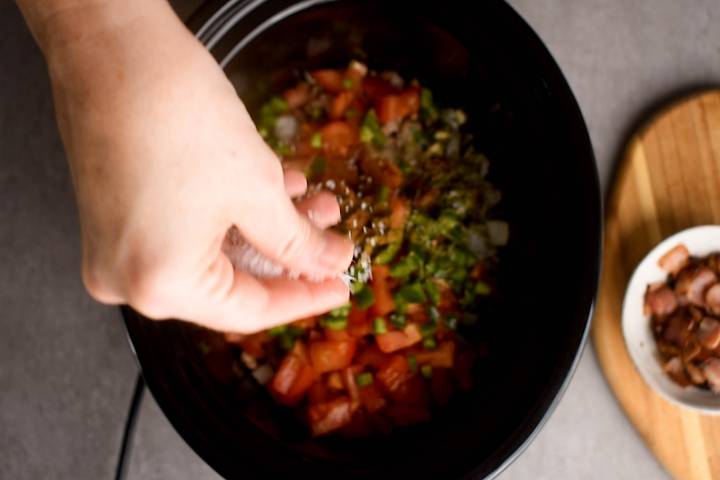 Spices being added to a slow cooker for charro beans.