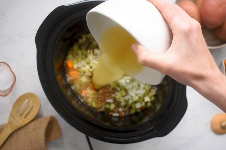 Ingredients for lentil soup with broth being poured on top in a slow cooker.