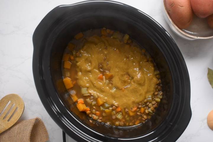 Blended lentil soup being added to a slow cooker.