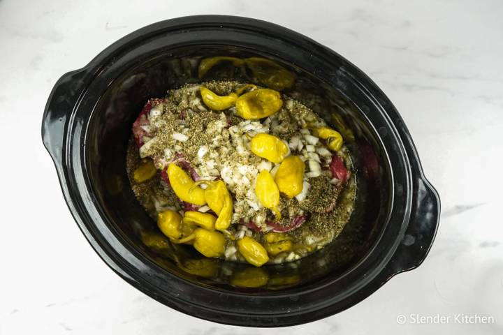 Beef in a slow cooker with pepperoncinis, onions, Italian seasoning, and beef broth.