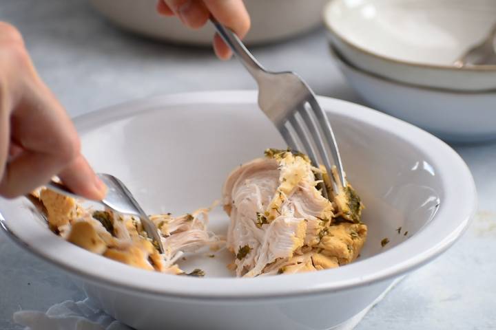 Pepperoncini chicken being shredded with two forks in a bowl.