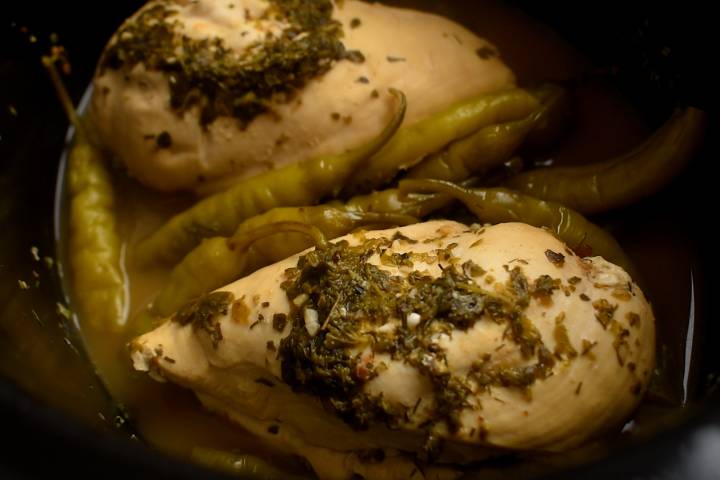 Chicken breast, pepperoncini peppers, Italian seasoning, and chicken broth in a slow cooker.