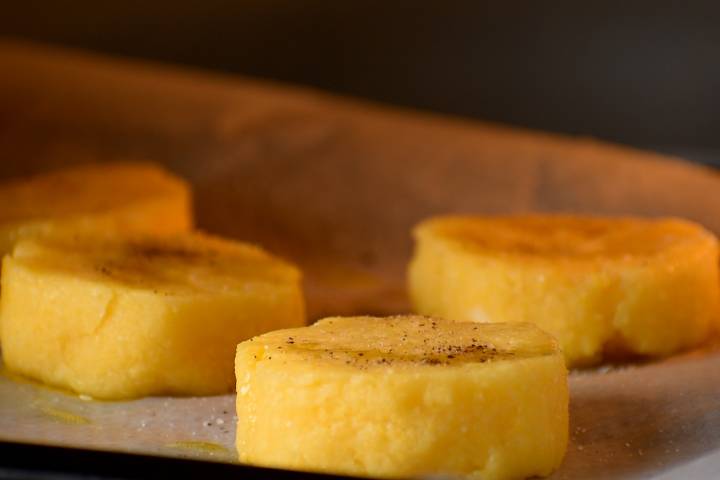 Polenta rounds baking in the oven with olive oil, salt, and pepper.