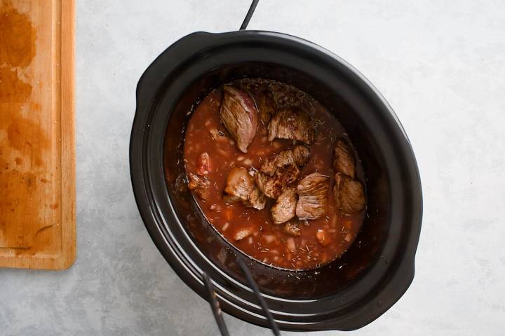 Beef, diced tomatoes, red wine, tomato paste, and seasoning in a slow cooker.