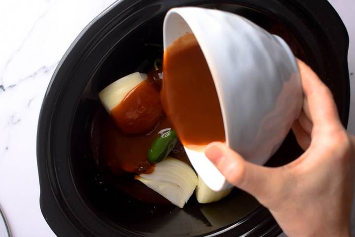 Onions, jalapenos, pork, and barbecue sauce in a slow cooker to make pulled pork.